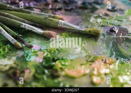 Künstler Pinsel und Ölfarben auf Holzpalette. Makrokünstler-Palette, Textur gemischte Ölfarben in verschiedenen Farben und Sättigung. Palette mit PA Stockfoto