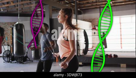 Überspringende Frau im hellrosa Tank, schwarze Leggings im Boxstudio, Sprungseil, Ring, DNA-Helix Stockfoto