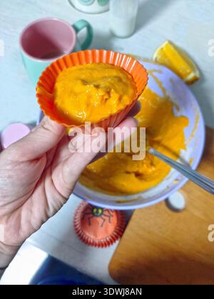Orangene Cupcakes machen – eine Silikonform mit Teig, Kürbissen, Karotten, Orangen. Halloween-Leckereien, bunte Kinderbackwaren Stockfoto