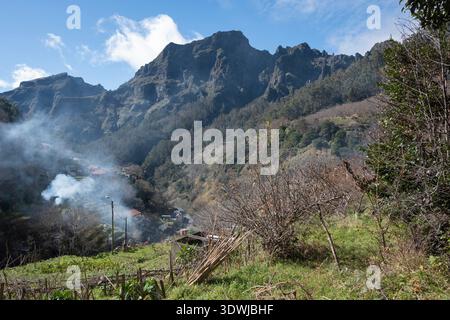 Terrassengärten und Wohnhäuser an einem steilen Hang vor felsigen Berggipfeln, Madeira, Portugal Stockfoto