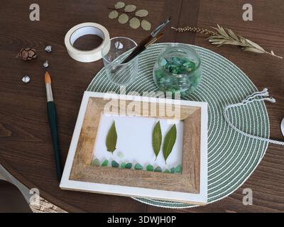 Gepresste und getrocknete Blätter im Rahmen. Glaskiesel, Naturmaterial, handgefertigtes Objekt auf dem Tisch. Hobbys und Lifestyle. Exotische mediterrane Pflanzen. Stockfoto