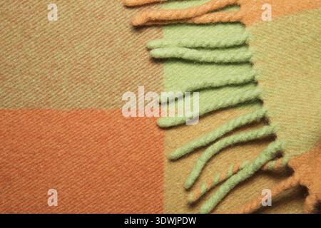 Weiche und warme gefaltete Alpaka-Wolldecke mit Fransen. Grün und orange Wolle karierten Textur Makro Schuss. Wolle karierter Stoff mit Fransen. Wolldecke Stockfoto