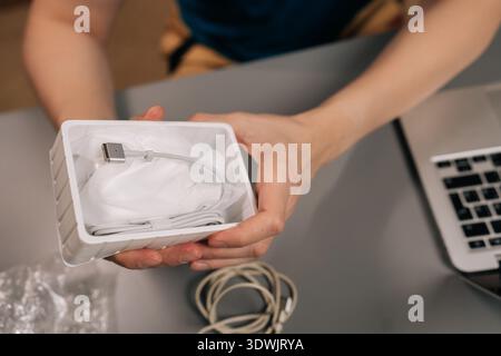 Person, die ein neu geöffnetes Paket mit usb-C-Ladekabel hält, Vorbereitung auf den Anschluss des neuen Zubehörs an einen Laptop auf dem Schreibtisch, Hervorhebung Stockfoto