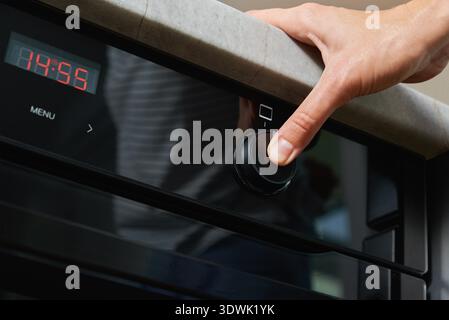 Weibliche Hand wählen Backprogramm auf elektrischen Ofen Bedienfeld, Frau mit elektrischen Ofen, moderne Haushaltsgeräte Stockfoto