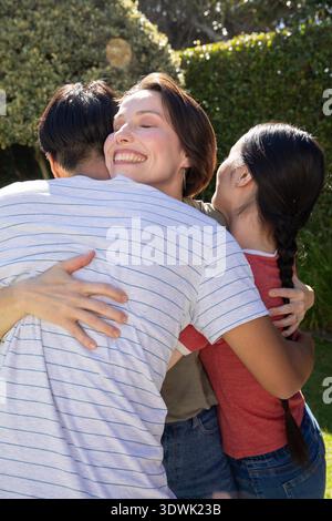 Vielfältige Familie, die sich im Garten in der Nähe von gepflegten Hecken unter Sonnenlicht umarmt. Familie, Vielfalt, Verbindung, Zuneigung, Outdoor, Harmonie, Ruhe || Model veröffentlicht Stockfoto