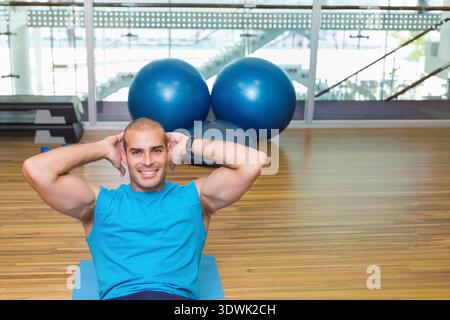 Mann mit blauem Workout Top, der Crunches auf blauer Matte im Fitnessstudio mit Stabilitätsbällen durchführt. Fitness, Core, Training, Athlet, Studio, atrium, Glas Stockfoto