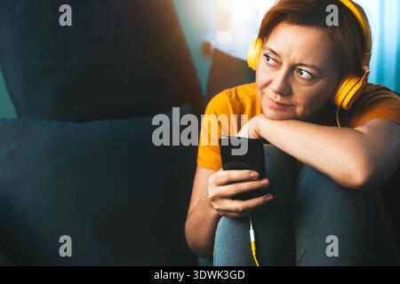Frau mit Kopfhörern zu Hause auf der Couch. Hören eines Podcasts oder einer Live-Übertragung. Entspannen Sie sich zu Hause. Das Konzept der Zeit für sich selbst, Seelenfrieden. Meditation mitten am Tag || Model wurde freigegeben Stockfoto