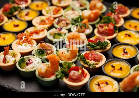 Eine große Auswahl an herzhaften kleinen Gebäckstücken, garniert mit Garnelen, Fleisch und farbenfrohen Moussen in ordentlichen Reihen. Stockfoto