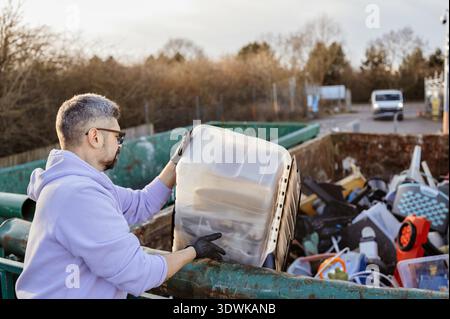 Mann, der große Plastikkiste im Freien in Recyclingbehälter entsorgt. Stockfoto