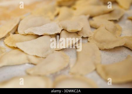 Ein Haufen ungekochter Teigknödel, wahrscheinlich Pierogi, sitzt auf einem weiß bemehlten Tisch. Die Knödel sind halbmondförmig mit gecrimpten Kanten, bereit für boi Stockfoto