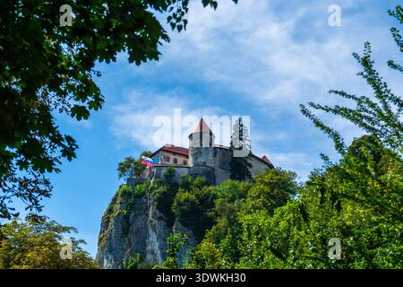 BLED, SLOWENIEN - 25. AUGUST 2025: Die slowenische Nationalflagge winkt von den Stadtmauern der Burg Bled auf einer Klippe über dem Bleder See. Stockfoto