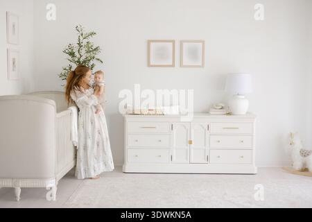 Mutter und Baby in einem hellen Kinderzimmer mit Olivenbaum und Krippe Stockfoto