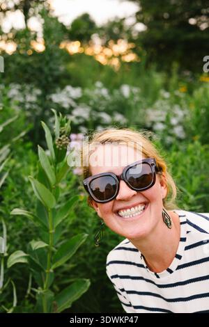 Erwachsene Frau in Sonnenbrille mit Sonnenuntergang und Wildblumenfeld Stockfoto