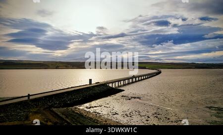 Aus der Vogelperspektive auf eine enge Straßenbrücke und einen Damm, der die Küstengewässer im Norden Schottlands unter dramatischem bewölktem Himmel überquert Stockfoto
