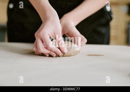 Junge Erwachsene Frau formt Ton mit Händen auf dem Tisch drinnen Stockfoto