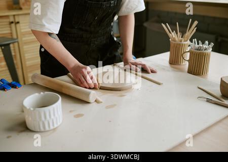 Junge Erwachsene Frau, die Ton auf dem Tisch in der Töpferwerkstatt formt Stockfoto