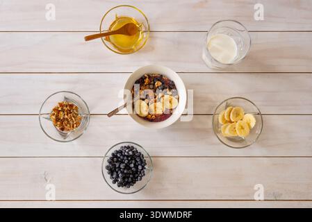 Fertiges Haferflocken mit Früchten und Nüssen umgeben von Rohstoffen, Konzept einer ausgewogenen Ernährung und gesundes Lifestyle-Frühstück Stockfoto