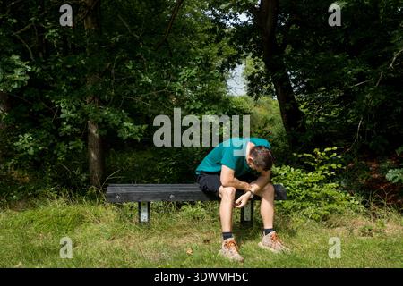 Mann mittleren Alters, der in foret auf der Bank sitzt, frustriert und besorgt, mit Händen im Gesicht Stockfoto
