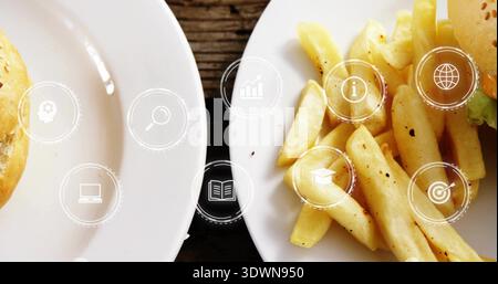 Weiße Teller mit gewürzten Pommes frites und Burgerbrötchen, Salat auf dunklem Tisch, digitale Symbole Stockfoto