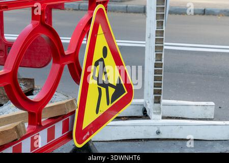 Das Schild informiert Fahrer über Straßenarbeiten in einem Stadtgebiet mit Barrieren und Materialien für Bauarbeiten. Stockfoto