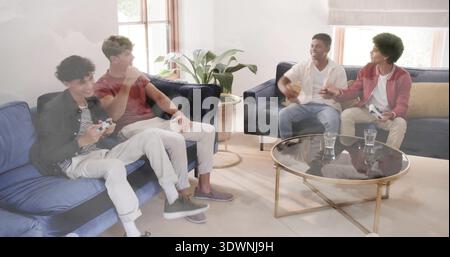 Vier Männer in lässigen Jacken und Jeans spielen, Spielecontroller auf Sofas in der Nähe des Glastisches halten Stockfoto