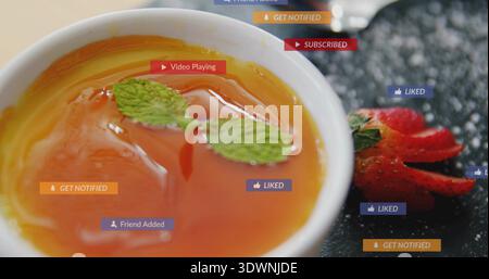 Weiße Tasse mit orangefarbener Flüssigkeit auf dem Tisch, Minze und Eis, in Scheiben geschnittene Erdbeeren, Benachrichtigungen Stockfoto