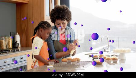 Pasping Frau und Kind Mädchen dekorieren Cupcakes auf der heimischen Kücheninsel, in Schürzen mit Paspelbeutel Stockfoto