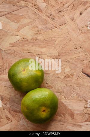 Mehrere Mandarinen, die von oben auf einem Holztisch betrachtet werden, schaffen eine lebendige, frische und rustikale Stillleben-Szene voller natürlicher Farben und Textur. Stockfoto