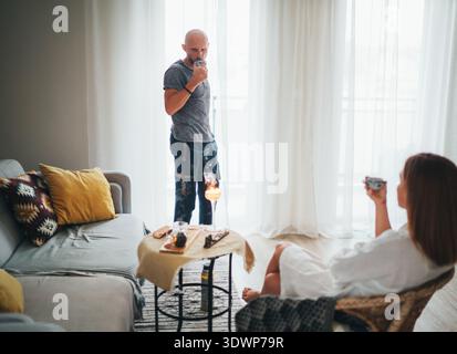 Glücklicher Mann mit Glatze, der im Rattan-Stuhl sitzt, genießt die traditionelle chinesische Gongfu Cha-Teezeremonie zu Hause und teilt warme frisch gebrühte Te Stockfoto