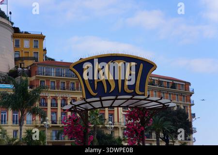 Großes blau-goldenes Schild 'CASTEL' in Nizza, Frankreich, mit Gebäuden des Hotels Suisse, Palmen, rosa Blumen und blauem Himmel darüber. Nizza, Frankreich Stockfoto