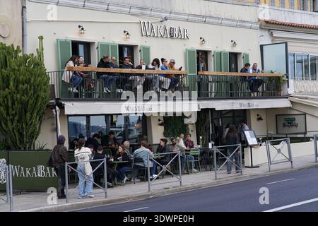 Auf dem Balkon und der Terrasse des Wakabar in Nizza, Frankreich, genießen die Menschenmassen Drinks mit grünen Fensterläden und ungezwungenen Sitzgelegenheiten im Freien entlang der Straße. Stockfoto