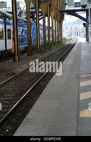 Sonnendurchfluteter historischer Bahnsteig am Gare de Nice Ville mit eleganten goldenen Säulen, verzierten Baldachinen und einem eleganten blauen Regionalzug Zou, der auf den Gleisen wartet. Stockfoto