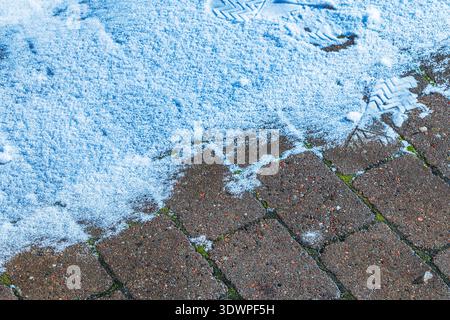 Nahaufnahme des schmelzenden Schnees auf Ziegelpflaster mit sichtbaren Fußabdrücken. Schweden. Stockfoto