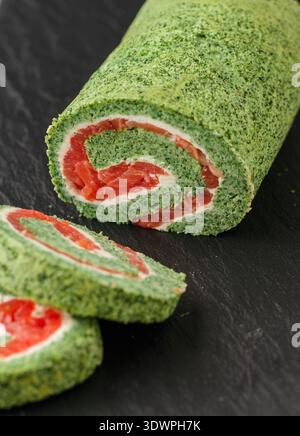 Geschnittene Spinatbrötchen mit gesalzenem (geräucherten) rotem Fisch (Lachs, Forelle) und Frischkäse (Ricotta) in Nahaufnahme. Roulette. Ein festlicher Snack für Gourmets. Christma Stockfoto