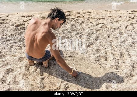 Ein Mann sitzt am Sandstrand von Cleopatra Beach in Alanya und ordnet kleine Kieselsteine sorgfältig in Form, Truthahn. Diese friedliche Szene Stockfoto