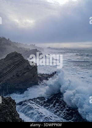 Wellen des Pazifischen Ozeans stürzen in der Abenddämmerung über die Sandsteinvorsprünge in der Nähe von Charleston, Oregon, USA Stockfoto
