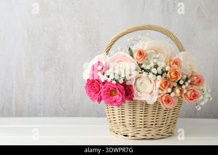 Schöne Blumen im Korb auf weißem Holztisch. Leerzeichen für Text Stockfoto
