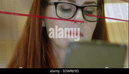 Liest rothaarige Frau mit schwarzer Brille, die im Büro Smartphone studiert, mit Datenüberlagerung Stockfoto