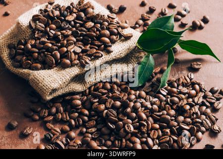 Sackleinen mit Kaffeebohnen und grünen Blättern auf dem Tisch. Draufsicht, flach Stockfoto