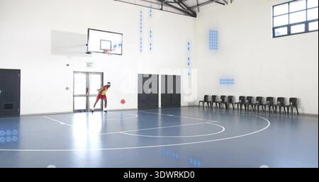 Tribbelnder männlicher Spieler in rot-gelbem Trikot auf dem Schulplatz mit orangem Basketball, Kopierraum Stockfoto