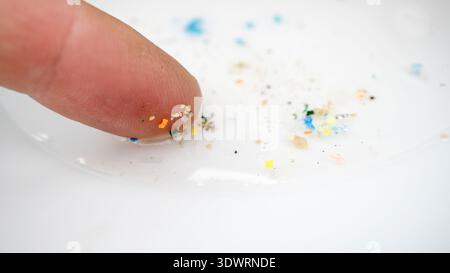Kleine Stücke Mikroplastik an der Fingerspitze. Diese Makroaufnahme zeigt den Umfang der Verschmutzung von Kunstfasern und Mikroplastik. Stockfoto