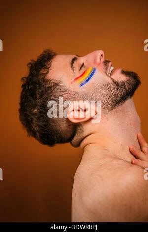 Bärtiger Mann mit Regenbogenfarbe auf der Wange, die Freude und Freiheit ausdrückt Stockfoto