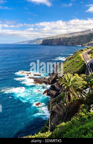 Malerischer, sonniger Blick auf die zerklüftete vulkanische Küste, blaue Wellen und die TF-31 Straße, die sich entlang der steilen Klippen in Puerto de la Cruz, Teneriffa, windet. Stockfoto