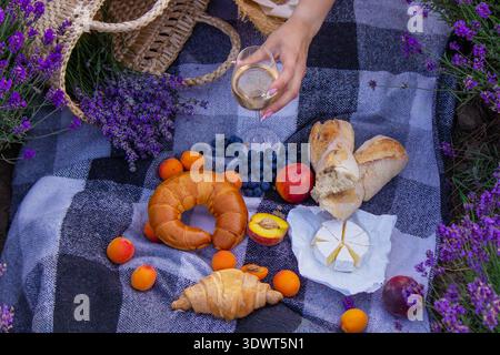 Ästhetisches Picknick in Lavendel: Wein, Obst, Käse und Croissants auf einer Decke Stockfoto