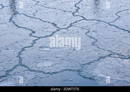 Abstrakte Nahaufnahme von strukturierten blauen Eisformationen und Kräuselungen auf einer teilweise gefrorenen See- oder Teichoberfläche. Das kalte Wasser erzeugt komplizierte Wellen p Stockfoto