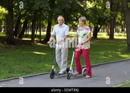 Seniorenpaar, das im Park mit einem Roller fährt. Active Seniors || Modell veröffentlicht Stockfoto