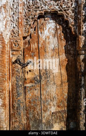 In Nako steht eine alte, verwitterte Holztür mit komplizierten Schnitzereien und einem Kettenschloss aus Metall als Zeugnis traditioneller Handwerkskunst. Stockfoto