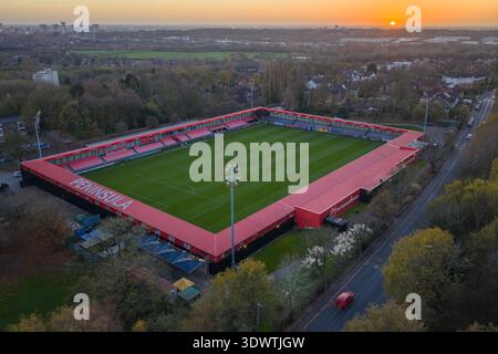 Luftbild des Peninsula Stadions, Heimstadion des Salford City FC, mit einem leuchtenden orangefarbenen Sonnenuntergang am Horizont über der Stadtlandschaft von Salford. Stockfoto