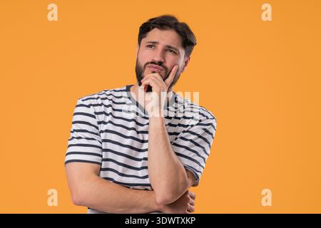 Nachdenklicher Mann, der aufblickt und auf Gelb nach Gelegenheiten sucht. Neugieriger bärtiger Kerl, der eine Lösung plant. Stockfoto