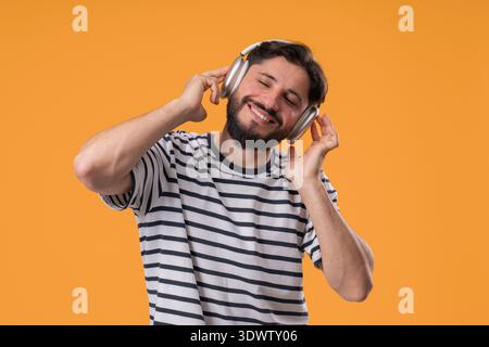 Bärtiger Mann, Der Mit Kabellosen Kopfhörern Auf Gelb Tanzt. Glücklicher Kerl, Tolle Stimmung Stockfoto